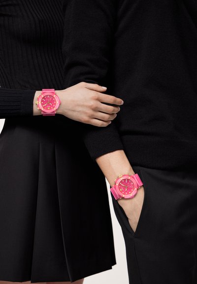 Kaks roosat kella kuldsete aktsentidega randmetel, millel on ümmargused sihverplaadid ja kummist rihmad, kantud musta riietusega.