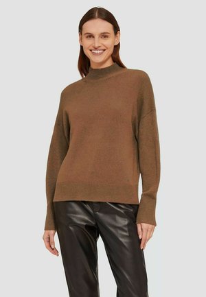 Brauner Strickpullover mit hohem Kragen und überschnittenen Schultern, kombiniert mit schwarzen Lederhosen. Die Textur wirkt weich und gemütlich.