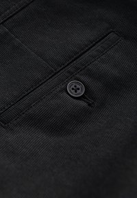 Tissu noir avec une surface texturée et un détail de bouton sur une poche. Le tissu présente un motif fin et est légèrement froissé.