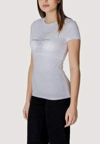 T-shirt bianco a maniche corte realizzato in un tessuto morbido ed elasticizzato, con un logo nero stampato "Armani Exchange" sul davanti. Design slim fit.