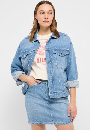 Woman wearing a light blue polka dot denim jacket with rolled sleeves and matching denim skirt, paired with a white graphic T-shirt.