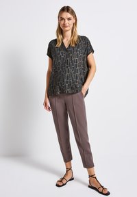 Blusa astratta nera e dorata con maniche corte abbinata a pantaloni croppati color marrone chiaro e sandali neri con cinturini.