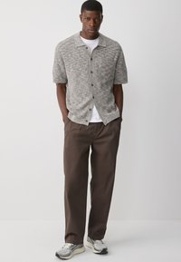 Grijze korte mouw cardigan met een gestructureerde brei, voorzien van een kraag en bruine knopen, gecombineerd met een paar loose-fit broeken in het bruin en grijze sneakers.