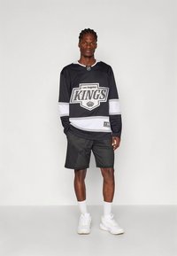Svart hockeytröja i mesh med "Los Angeles KINGS"-logotyp, vita detaljer, tillsammans med svarta meshshorts och vita sportskor.