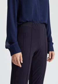 Marineblouse met doorzichtige manchetten, gecombineerd met aansluitende marinebroeken met zijzakken en een gladde textuur.