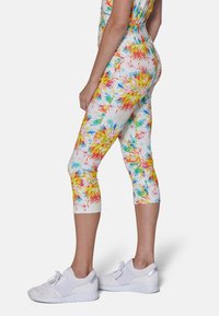 Värikäs, sopiva capri legginsit kukkakuviolla, jossa on keltaista, punaista ja sinistä valkoista taustaa vasten. Valmistettu joustavasta kankaasta.