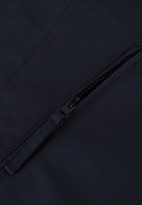 Marineblauwe stof met een gladde textuur, voorzien van een ritszak. De rits is zwart, met zichtbare stiksels langs de randen.