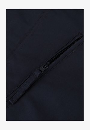 Marineblauwe stof met een gladde textuur, voorzien van een ritszak. De rits is zwart, met zichtbare stiksels langs de randen.
