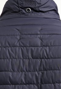 Giacca trapuntata blu navy sul retro con cuciture orizzontali, texture imbottita e un'etichetta con il logo "Camel Active" vicino al colletto.