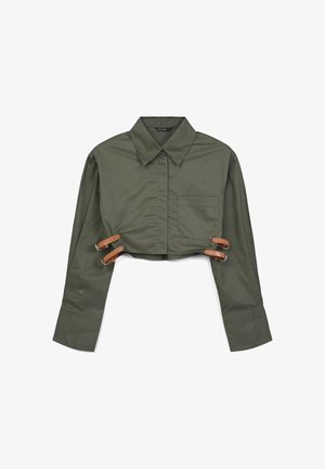 Gekürztes olivgrünes Hemd aus glattem Stoff, mit spitzem Kragen, einer Brusttasche und Lederriemen mit metallischen Clips an den Seiten.