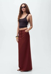 Črn rebrast crop top, burgundska maxi krila z bočnimi žepi, gladka tekstura in ravne sandale. Model nosi sončna očala in zapestnico.