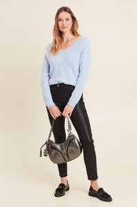 Maglione fuzzy blu chiaro, jeans neri attillati, mocassini neri in vernice e una borsa a tracolla metallica con catena e nappina decorativa.