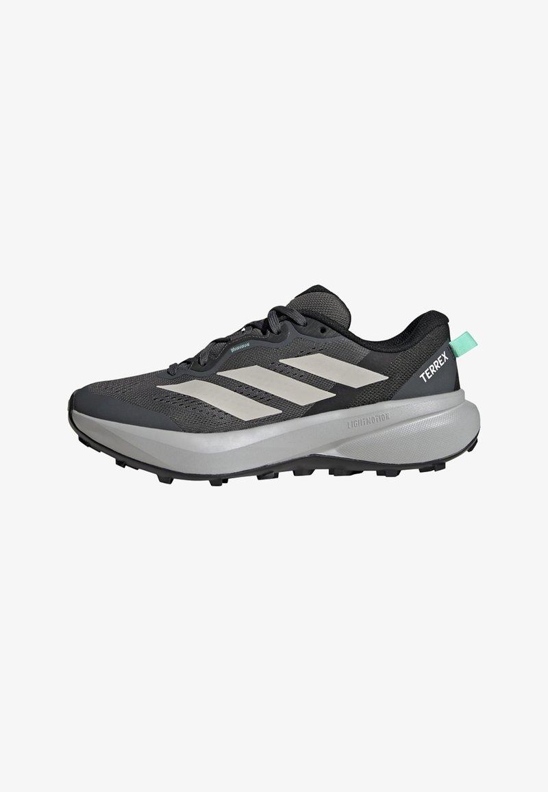 Μαύρο και γκρι παπούτσι ορεινού τρεξίματος Adidas Terrex με λευκές ρίγες, παχιά επενδεδυμένη σόλα και τυρκουάζ λουράκι στο πίσω μέρος.