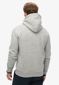 Felpa grigia con cappuccio realizzata in tessuto testurizzato, caratterizzata da una vestibilità ampia, polsini a coste e un cappuccio spesso. Design minimalista senza motivi.
