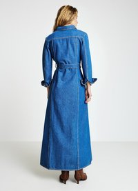 Robe maxi en denim avec un col à revers, une taille ceinturée, des manches longues et des poches latérales. Présente des coutures apparentes et une texture lisse.
