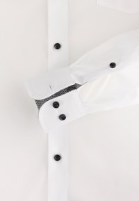 Das weiße Hemd hat lange Ärmel, schwarze Knöpfe und eine gemusterte Akzentuierung im Inneren der Manschetten. Glattes Gewebe mit einem klaren Finish.