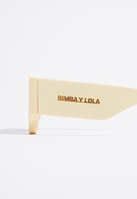 Gafas de sol color crema con un acabado suave, que presentan un audaz logo "BIMBAY LOLA" en dorado en la patilla.