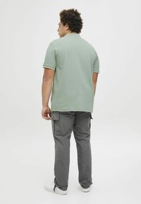 Grøn tekstureret polo med kontrastkrave, parret med grå cargo-bukser med sidelommer og hvide sneakers. Bagfra synlig.