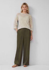 Maglione lavorato a maglia color beige chiaro con trama aperta e maniche a tre quarti, abbinato a pantaloni larghi di colore verde oliva. Orecchini d'oro e sandali.
