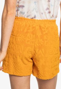 Pomarańczowe bawełniane szorty z teksturowanymi wzorami, zawierające motywy kwiatowe i geometryczne, z elastycznym pasem dla wygody.