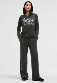 Dark gray long-sleeve top with white graphic text paired with matching wide-leg pants. Soft, textured fabric. Black footwear completes the outfit.