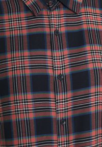 Rotes, marineblaues und weißes kariertes Hemd mit Button-Down-Kragen, schwarzen Knöpfen und einer strukturierten Stoffqualität mit kontrastierenden Mustern.