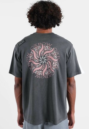 T-shirt en coton gris foncé avec un motif graphique spirale en rose et noir au dos, avec un patch logo sur l'épaule.