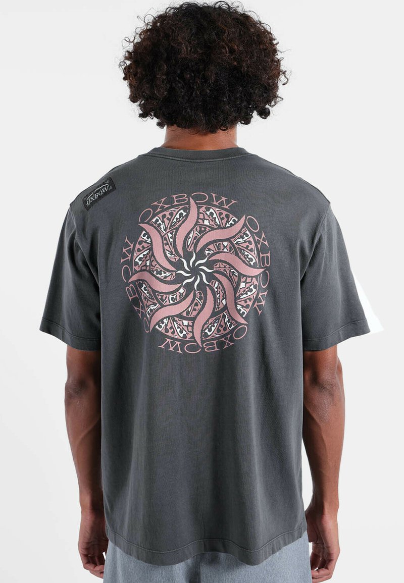 T-shirt en coton gris foncé avec un motif graphique spirale en rose et noir au dos, avec un patch logo sur l'épaule.