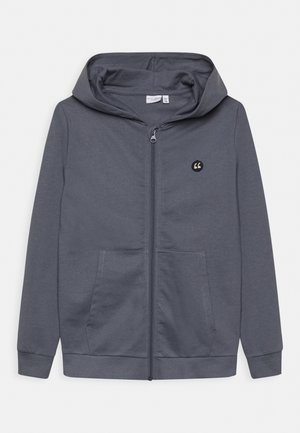 Szara bluza z kapturem zapinana na zamek, wykonana z miękkiego materiału, z przednim zamkiem błyskawicznym, dwoma kieszeniami oraz kapturem, z małym logo na górnej lewej stronie.