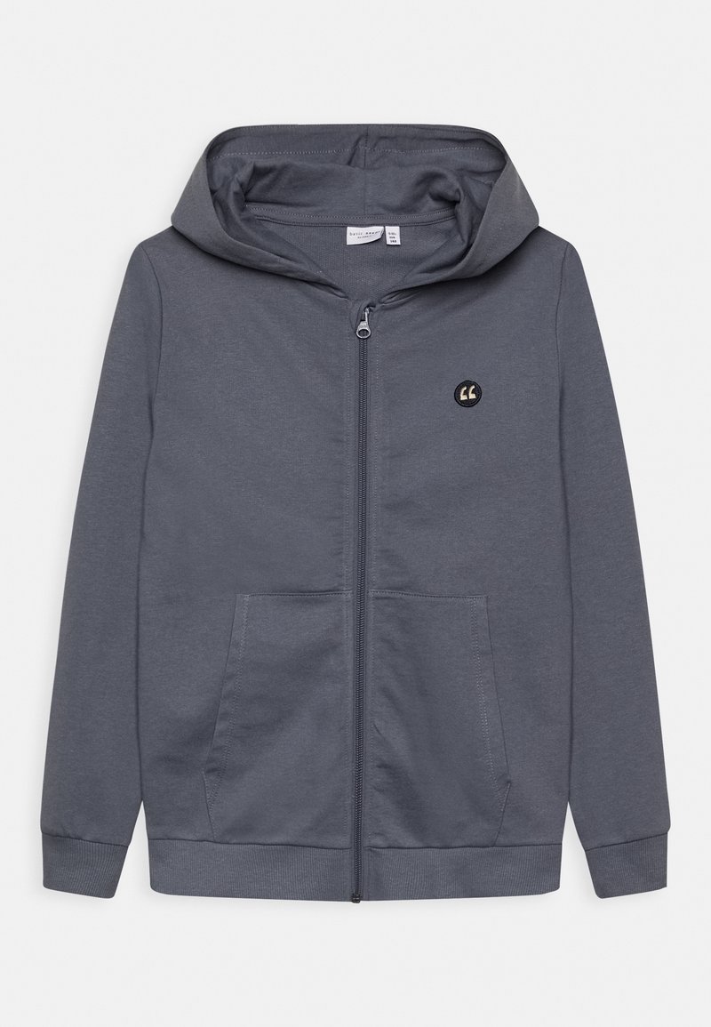 Sweat à capuche gris zippé en tissu doux, avec une fermeture éclair à l'avant, deux poches et une capuche, orné d'un petit logo sur le haut à gauche.