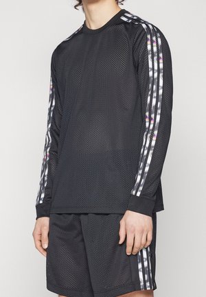 Personne portant une chemise noire en maille à manches longues et un short assorti avec des détails rayés argent brillant et noir sur les manches et les côtés.