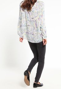 Blusa a maniche lunghe con motivo paisley nei colori pastello; tessuto leggero, taglio rilassato, abbinata a pantaloni neri e scarpe basse.