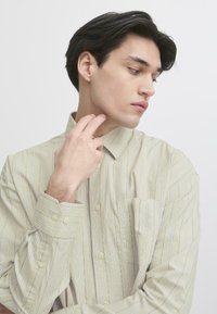 Lys beige stripete skjorte med klassisk krage og frontlomme. Har myk stoff og knapper på ermene.