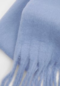 Écharpe en laine bleu clair avec une texture douce, un éclat subtil et des bords frangés. Le matériau semble léger et chaud avec une finition lisse.