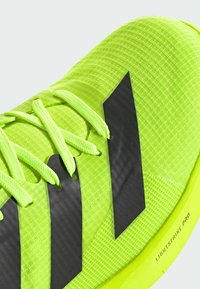 Scarpa da ginnastica sportiva di un verde neon acceso con tomaia testurizzata, accenti neri e design leggero. Dettagli includono lacci sottili e marchio.