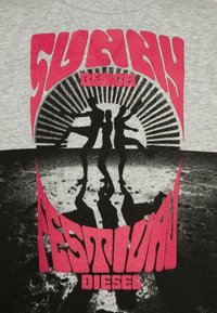 Tři siluety postav tančících na pláži se slunečními paprsky za nimi a tučný červený text "Sluneční plážový festival Diesel."
