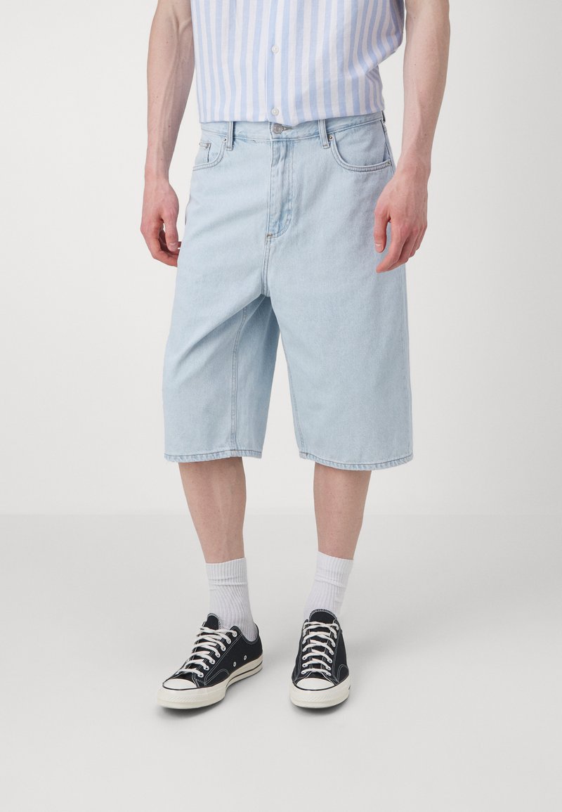 Light blue denim shorts with a relaxed fit, knee-length cut, and five-pocket design. Paired with black sneakers and white socks.