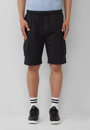 Shorts cargo noirs avec une taille élastique, des poches latérales et une texture lisse, associés à des baskets noires et des chaussettes blanches rayées.