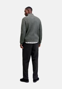 Gray ribbed sweater with a high collar, paired with black trousers. The model's back is shown, highlighting the fabric's texture and fit.