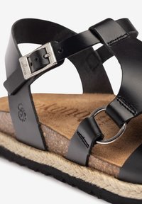 Sandali in pelle nera con cinturini incrociati, fibbia in argento e insole in sughero. Presentano una soletta intermedia in juta testurizzata e una suola in gomma.