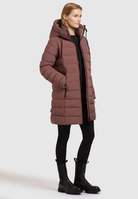 Mīksts mētelis ar kapuci, lavandas krāsā. Ar rāvējslēdzēja kabatām, taisnu piegriezumu un spīdīgu apdari. Kombinēts ar melnajām legingām un zābakiem.