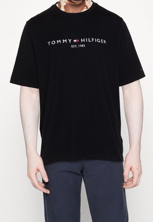 Schwarzes Baumwoll-T-Shirt mit kurzen Ärmeln, auf der Vorderseite mit dem "TOMMY HILFIGER" Logo und "EST. 1985" in kontrastierenden Farben bedruckt.