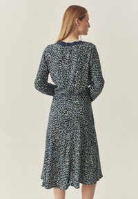 Rochie cu mâneci lungi, de culoare bleumarin, cu un model dispersat de nuanțe de albastru deschis și bej. Prezintă o talie ajustată și o fustă fluidă. Textură de țesătură netedă.