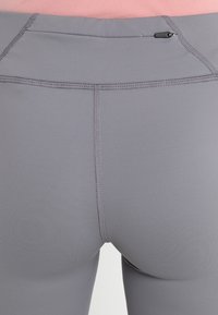 Graue Leggings aus elastischem Material. Mit Flachnaht-Nähten, hohem Bund und einer kleinen Tasche auf der Rückseite für zusätzlichen Komfort.