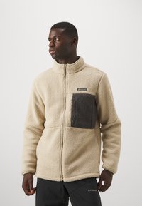 Kerman fleece-takki, jossa on korkea kaulus ja tumma harmaa rintatasku. Varustettu täysipitkällä vetoketjulla ja teksturoidulla materiaalilla.