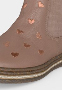 Gros plan d'une chaussure en cuir marron avec de petits cœurs brodés et une semelle épaisse texturée avec détail de couture.