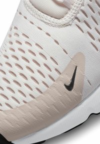 Ľahká teniska v bielej a béžovej farbe s textúrovaným sieťovinovým zvrškom, perforovanými detailmi a čiernym logom Nike po boku.