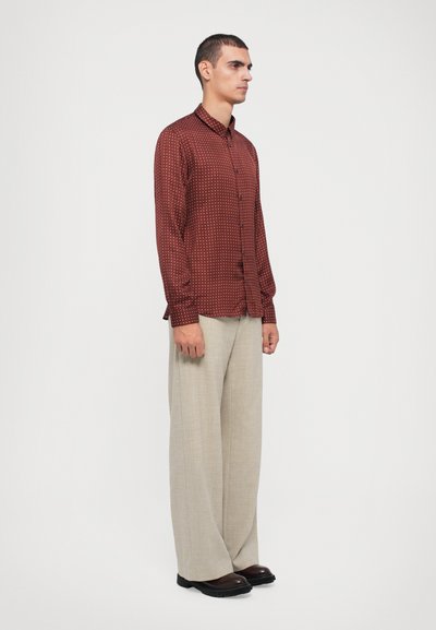 Brown patterned long-sleeve shirt with a collar, button-down front, paired with light beige wide-legged trousers and dark shoes.