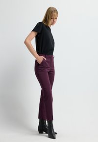 Top noir à manches courtes associé à un pantalon moulant bordeaux avec des poches latérales et une légère fente à l'ourlet. Porté avec des bottines noires.