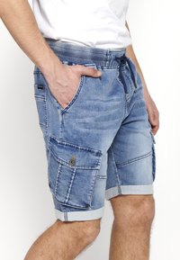 Lys blå denimshorts med elastisk talje, snøre lukning, sidelommer og en cargo lomme. Omslag ved kanten.